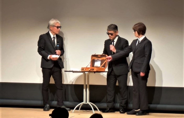 三人が白い粉を囲んで話す様子